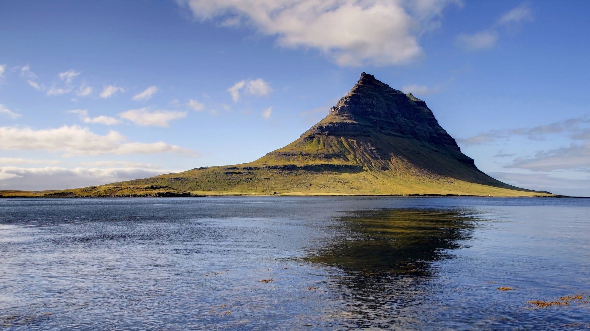 Der markante Berg Kirkjufell in Island spiegelt sich im ruhigen Wasser des Fjords bei Grundarfjörður.