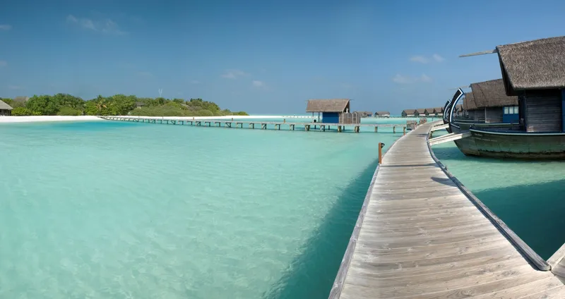 Holzsteg führt zu Überwasserbungalows in einer türkisfarbenen Lagune auf den Malediven.