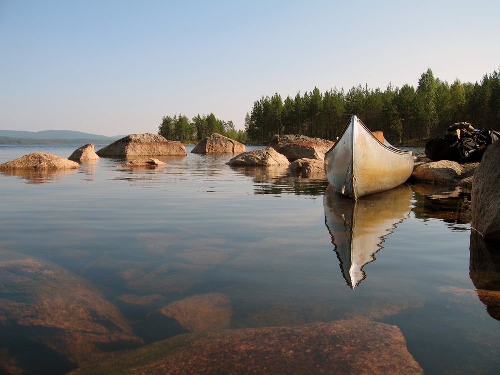 Kanu liegt an einem felsigen Seeufer in der schwedischen Wildnis zwischen Nadelbäumen im Abendlicht.
