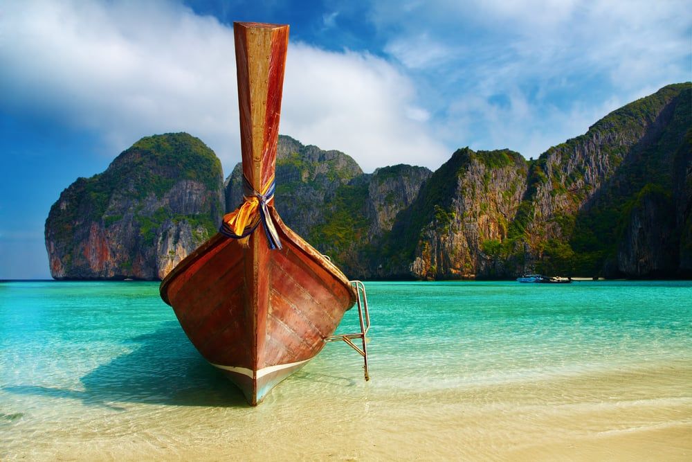 Traditionelles Longtailboot an der türkisfarbenen Lagune der Maya Bay in Thailand mit Kalksteinfelsen im Hintergrund.